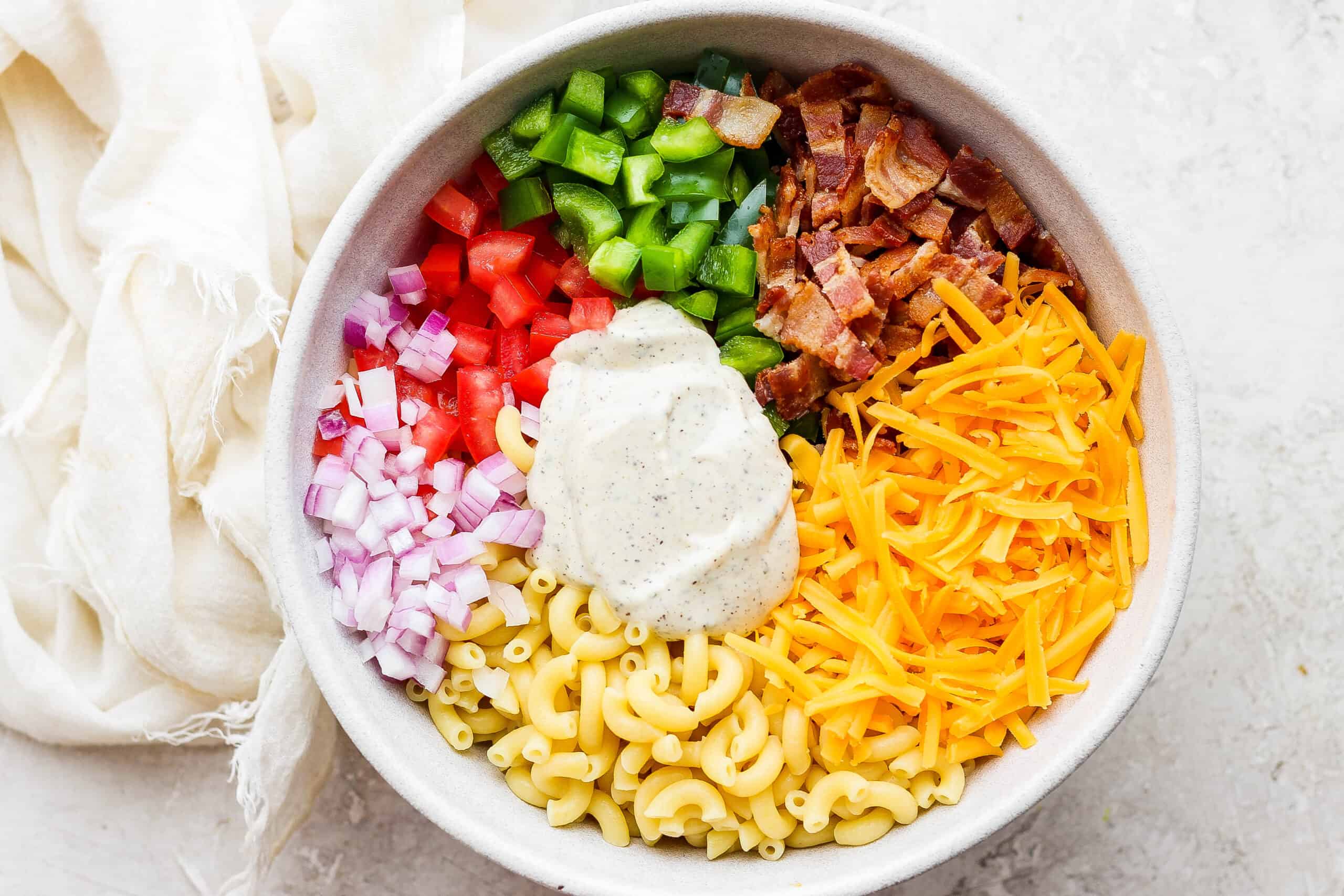 Dressing is shown on top of a white bowl of bacon ranch pasta salad.