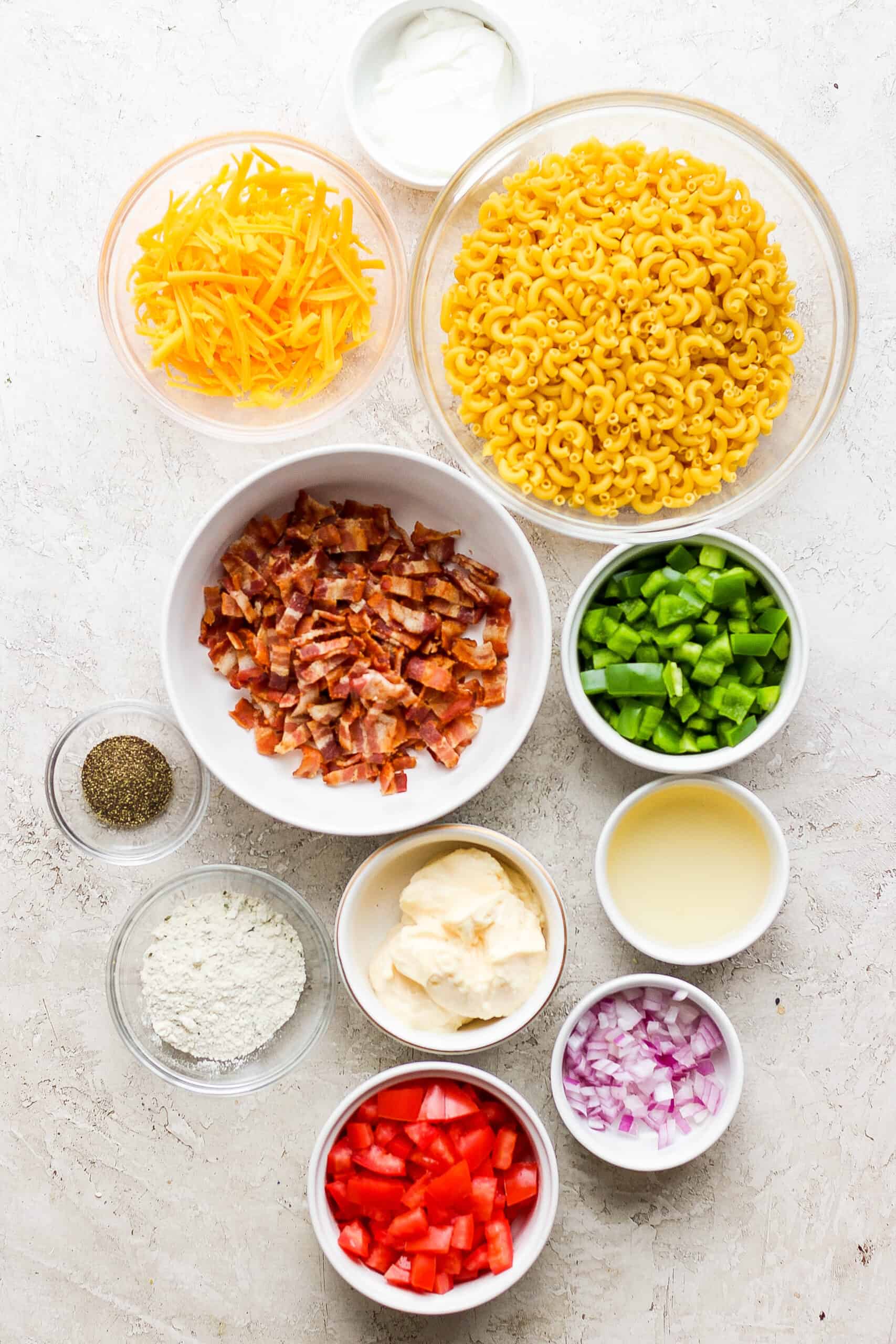 Ingredients for bacon ranch pasta salad: green onions, red onions, macaroni, cheddar cheese, pepper, and bacon.