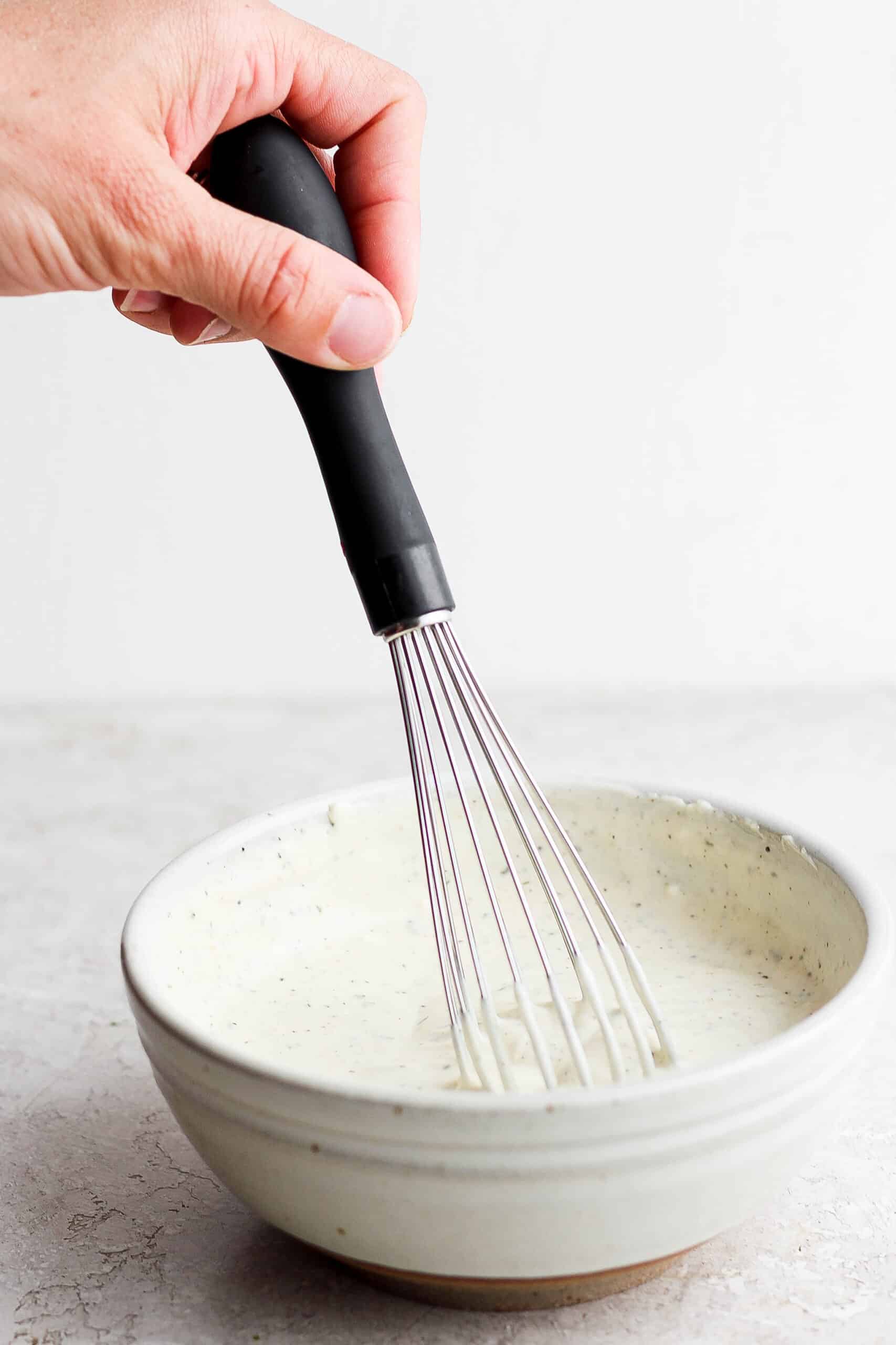 A hand whisks dressing in a bowl.