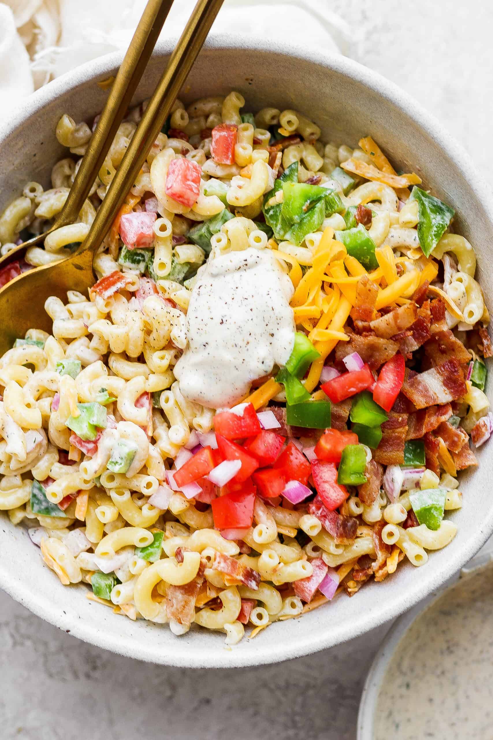Make this crowd-pleasing Bacon Ranch Pasta Salad for your next bbq! Crispy bacon, and tender pasta will make this potluck side a new favorite. Mixing vegetables and macaroni together in a bowl.