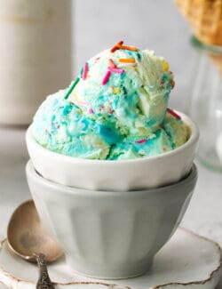 A bowl of blue birthday cake ice cream with a cone of ice cream next to it.