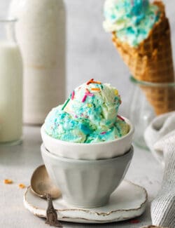 A bowl of blue birthday cake ice cream with a cone of ice cream next to it.