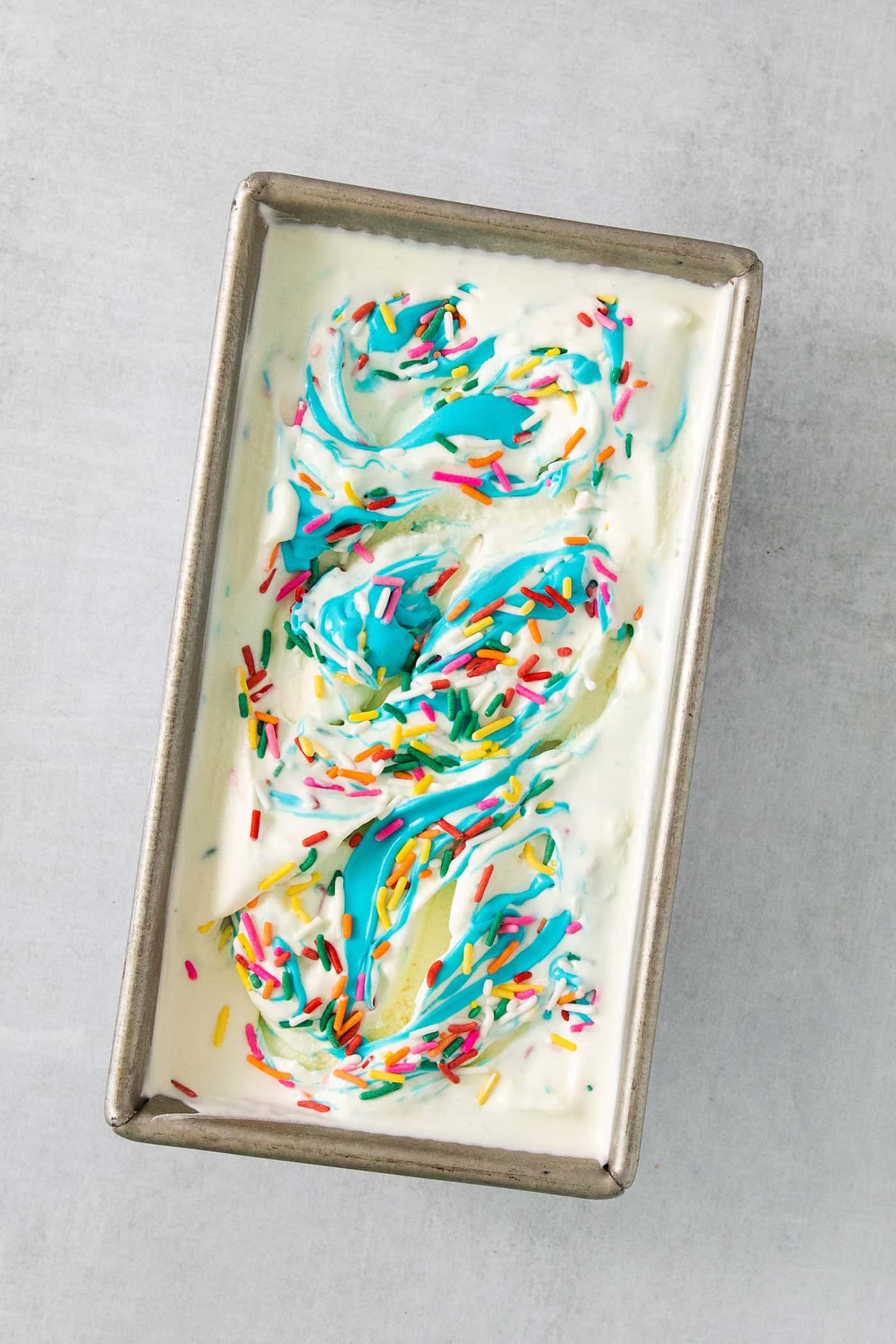 A loaf pan with birthday cake ice cream topped with blue frosting and sprinkles.