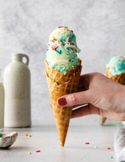 A hand holds a cone of birthday cake ice cream.