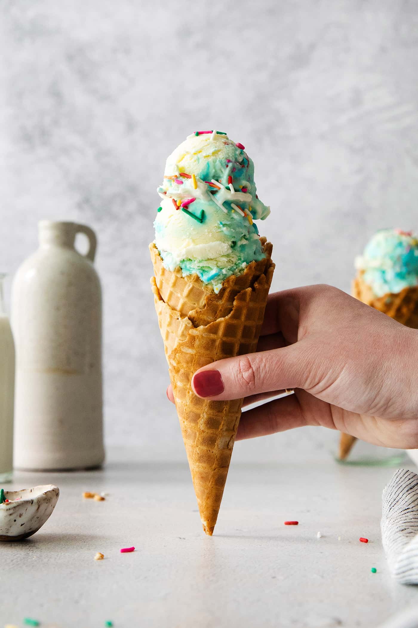 A hand holds a cone of birthday cake ice cream.