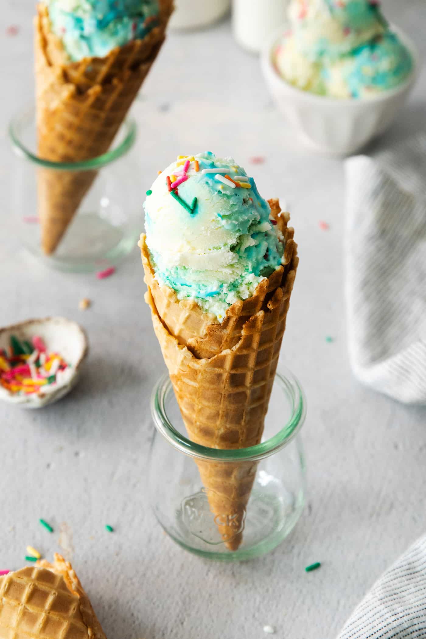 Birthday cake ice cream cones with rainbow sprinkles alongside.