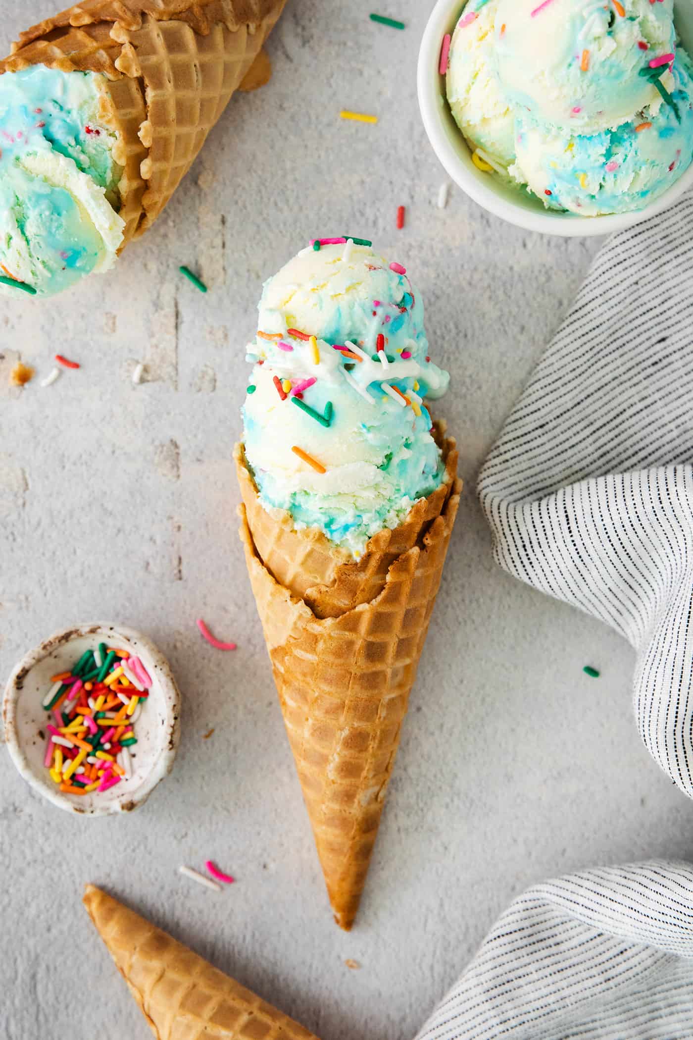 Birthday cake ice cream cones with rainbow sprinkles alongside.
