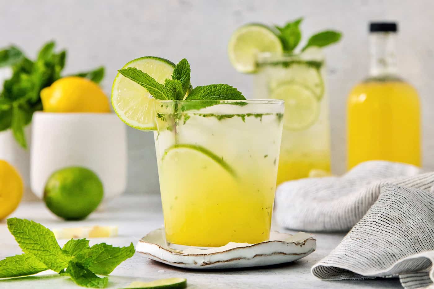 A bootleg cocktail in a glass with mint and lime circles with fruit juice in the background.