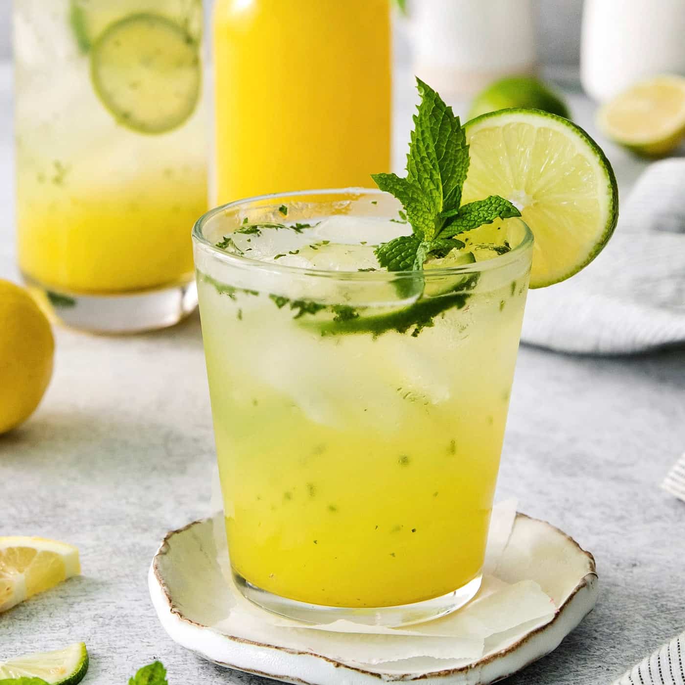 A bootleg cocktail in a glass with mint and lime circles with fruit juice in the background.