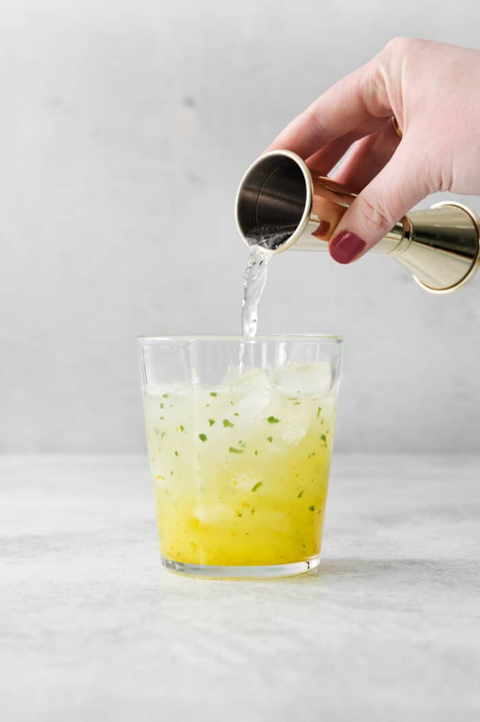 Club soda is poured into a glass of yellow fruit juice, vodka, and ice.