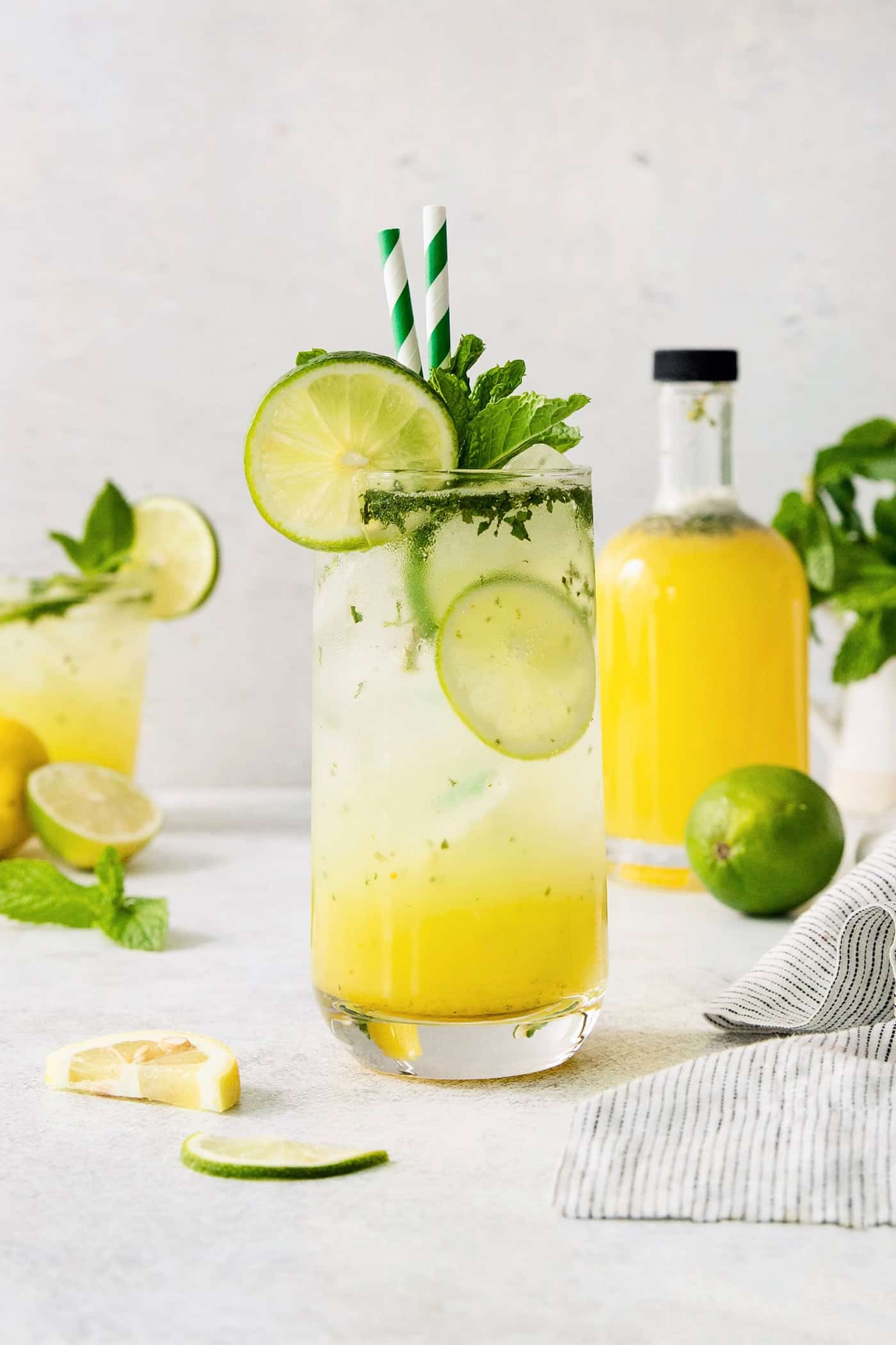 A bootleg cocktail in a glass with straws and lime circles with fruit juice in the background.