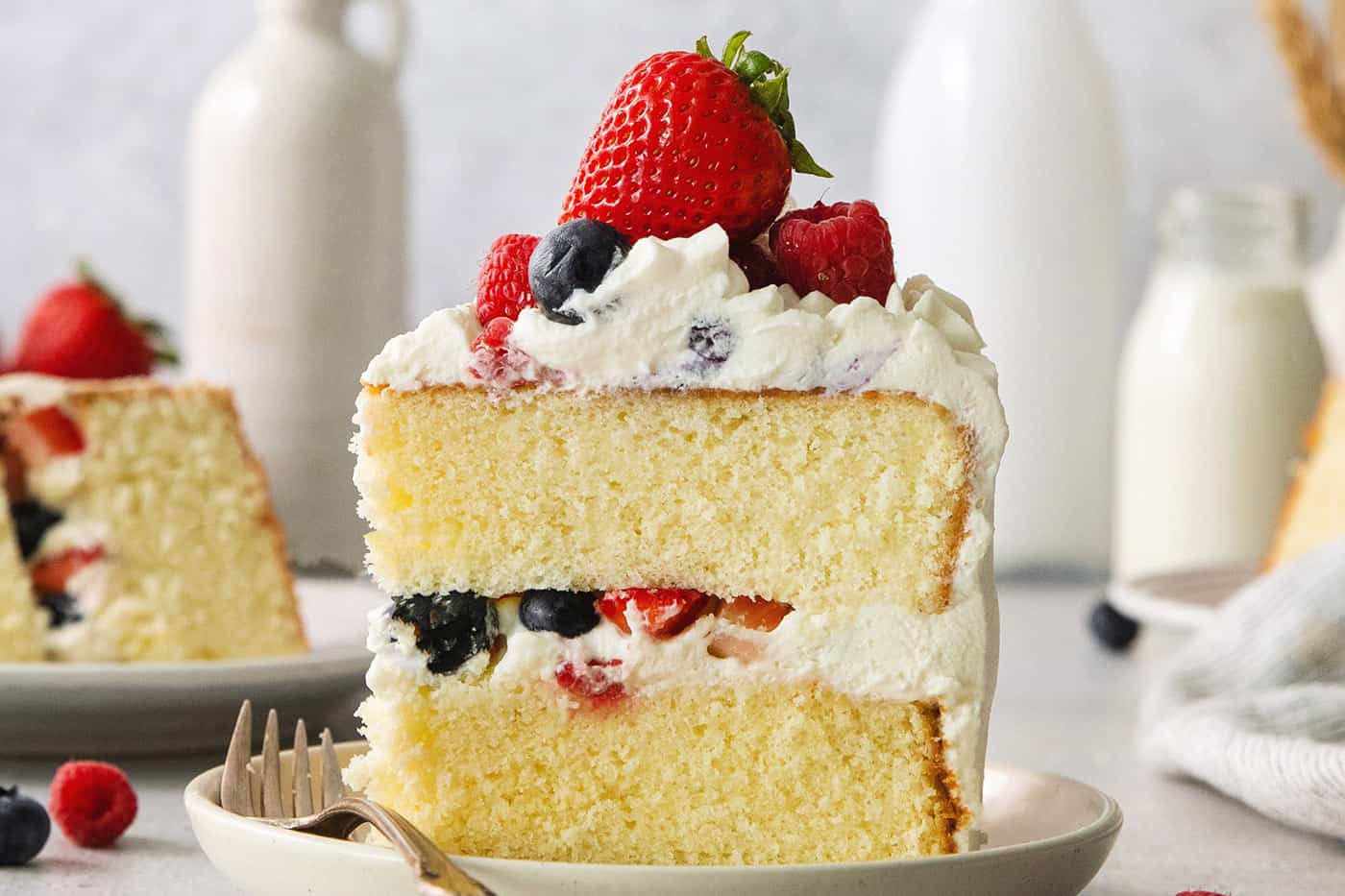 A slice of berry Chantilly cake on a plate with a fork.