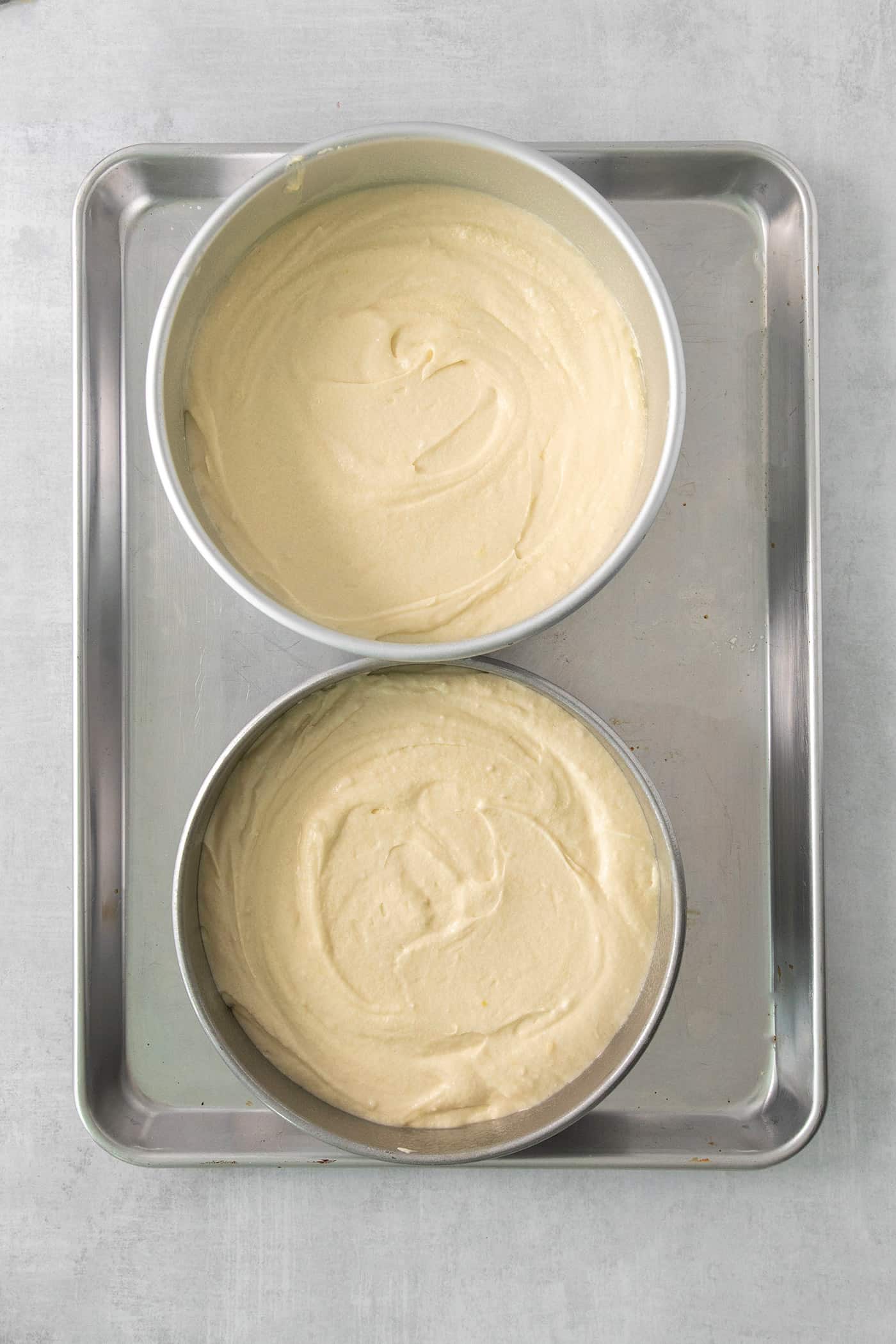 Cake pans filled with batter on a baking sheet.
