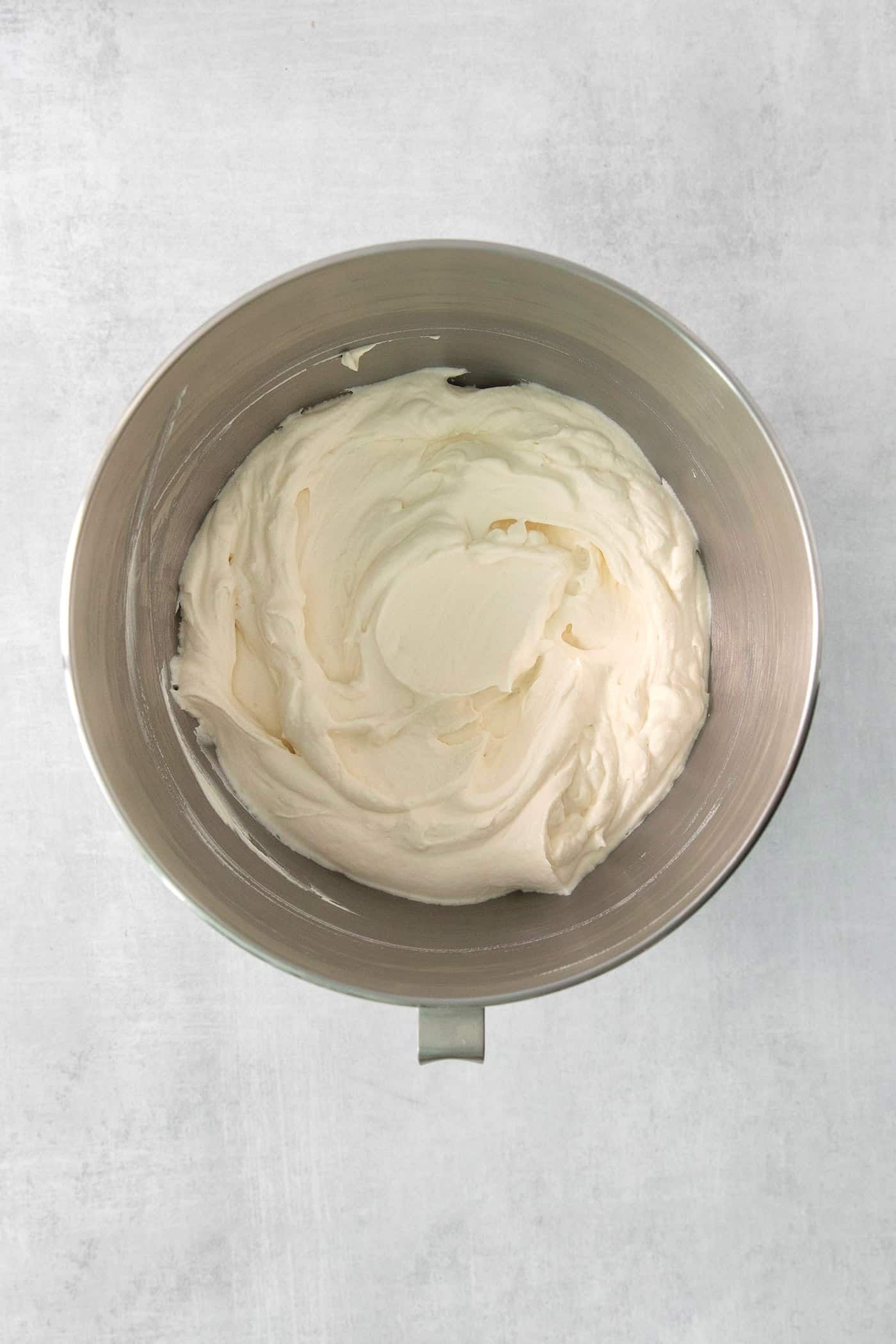 Whipped Chantilly cream is shown in the bowl of a stand mixer.
