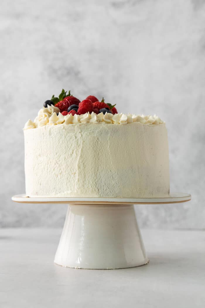 A Chantilly cake on a white cake stand topped with berries.