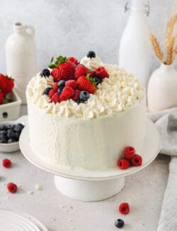 A Chantilly cake on a white cake stand topped with berries.