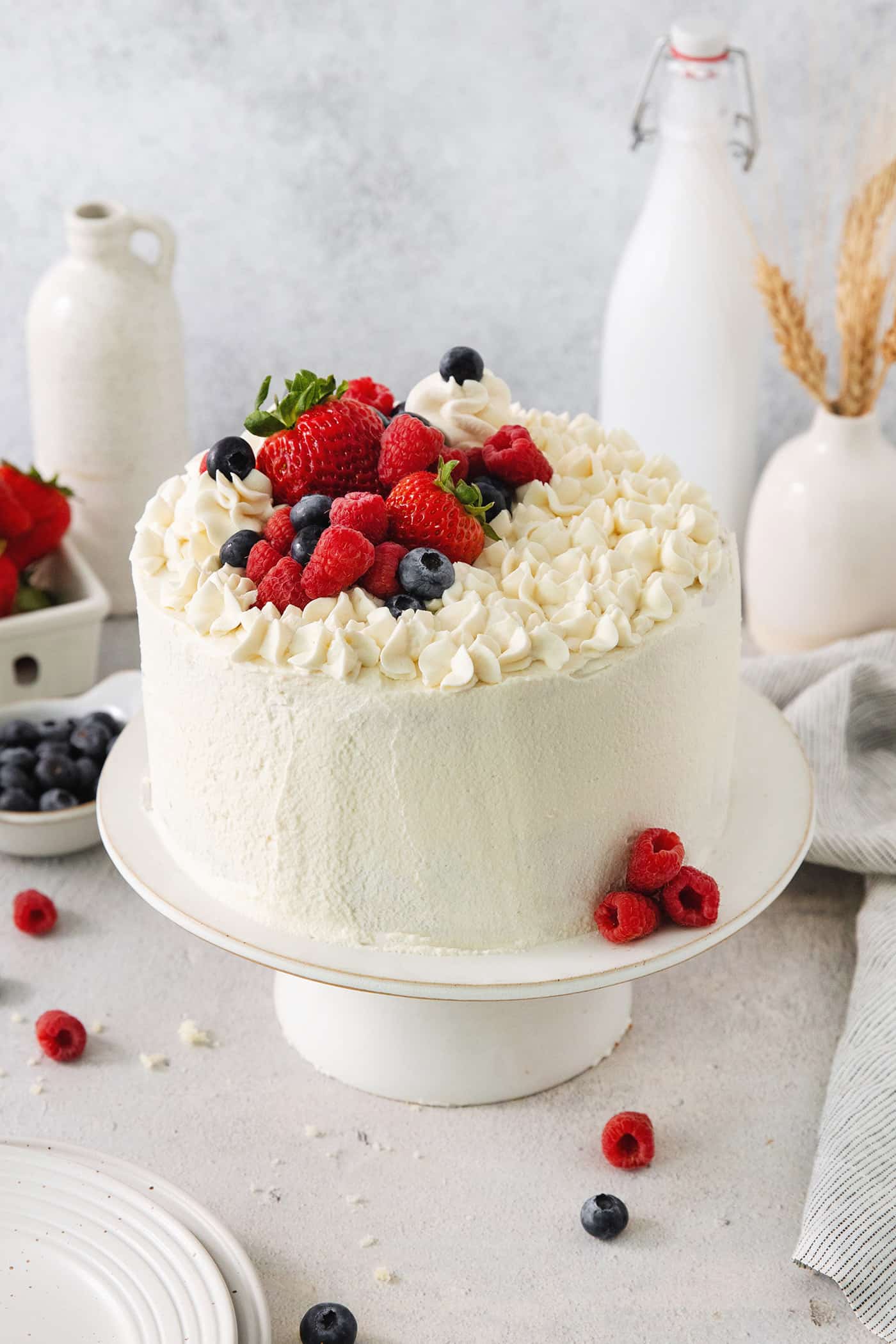 A Chantilly cake on a white cake stand topped with berries.