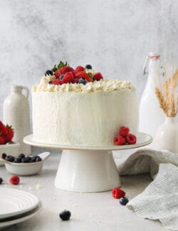 A Chantilly cake on a white cake stand topped with berries.