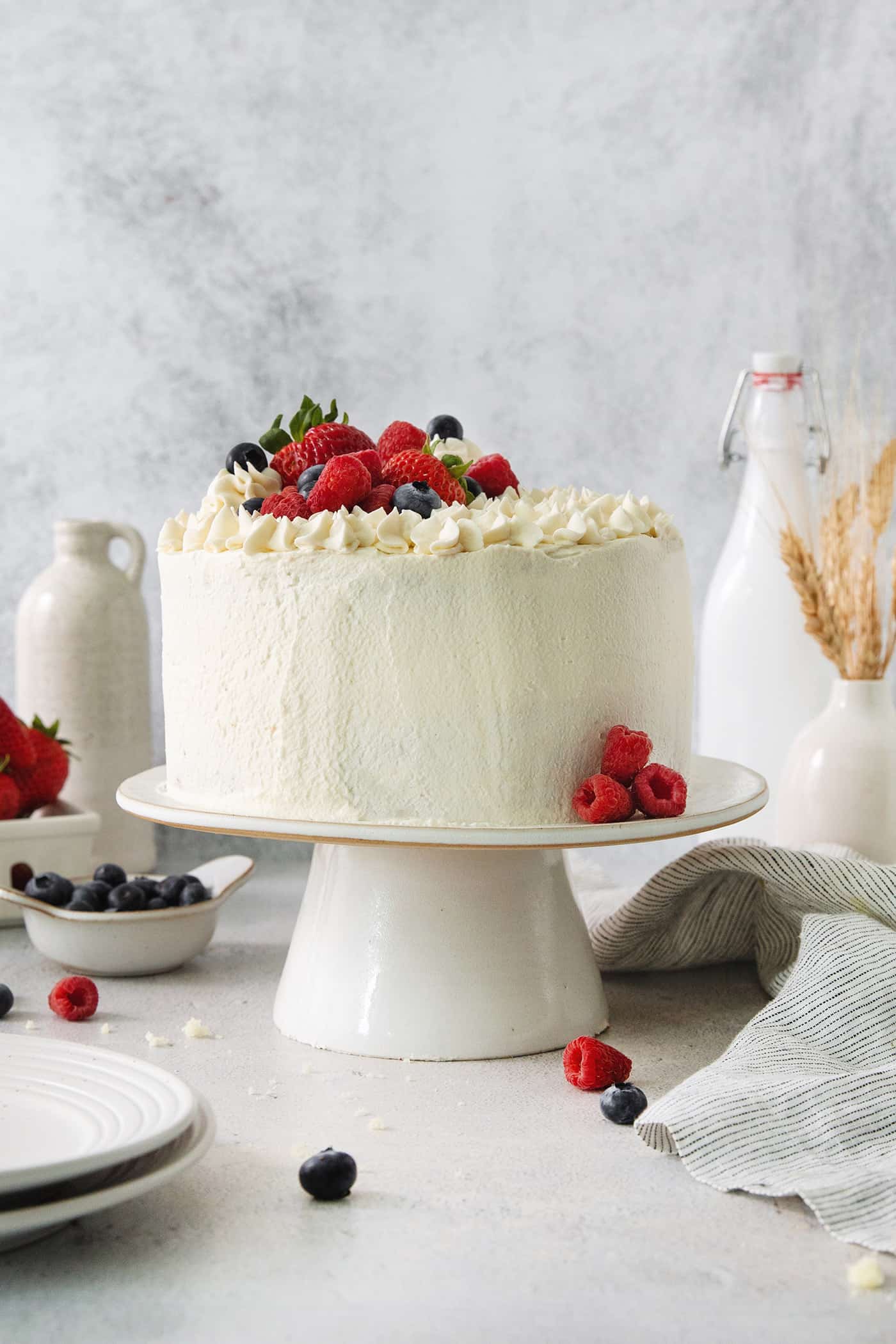 A Chantilly cake on a white cake stand topped with berries.
