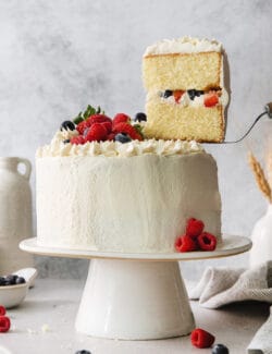 A Chantilly cake on a white cake stand with a slice cut out.