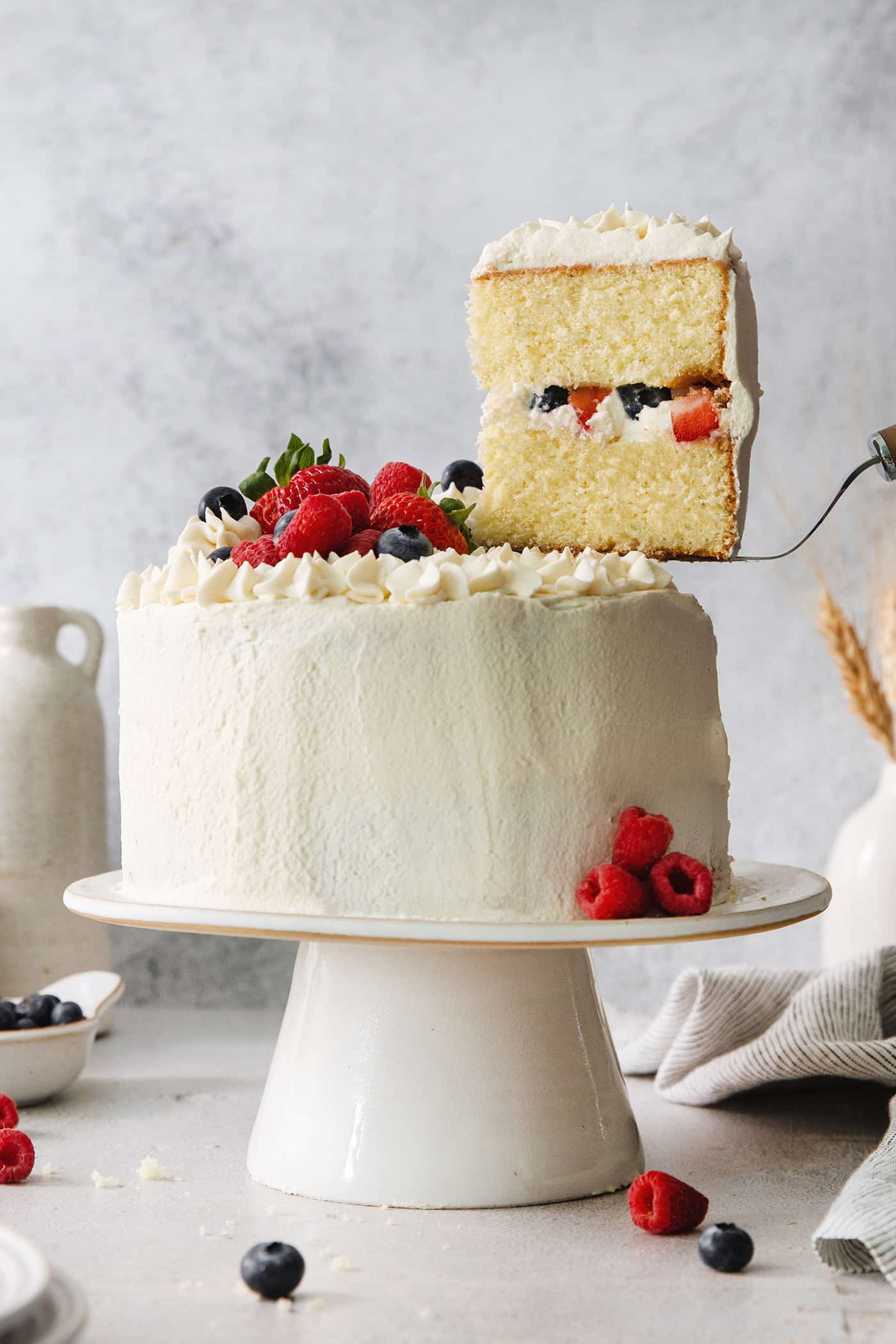 A Chantilly cake on a white cake stand with a slice cut out.