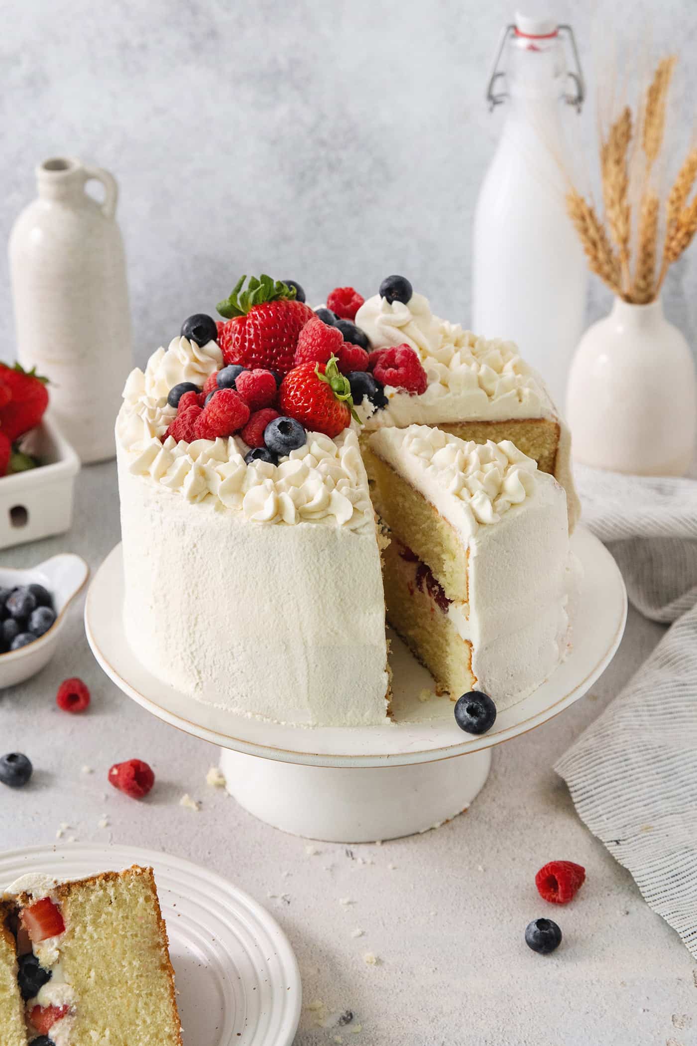 A Chantilly cake on a white cake stand with a slice cut out.