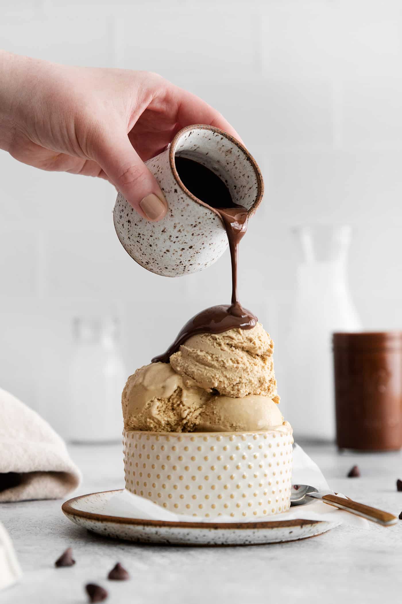 A hand pours a pitcher of magic shell over a bowl of ice cream.