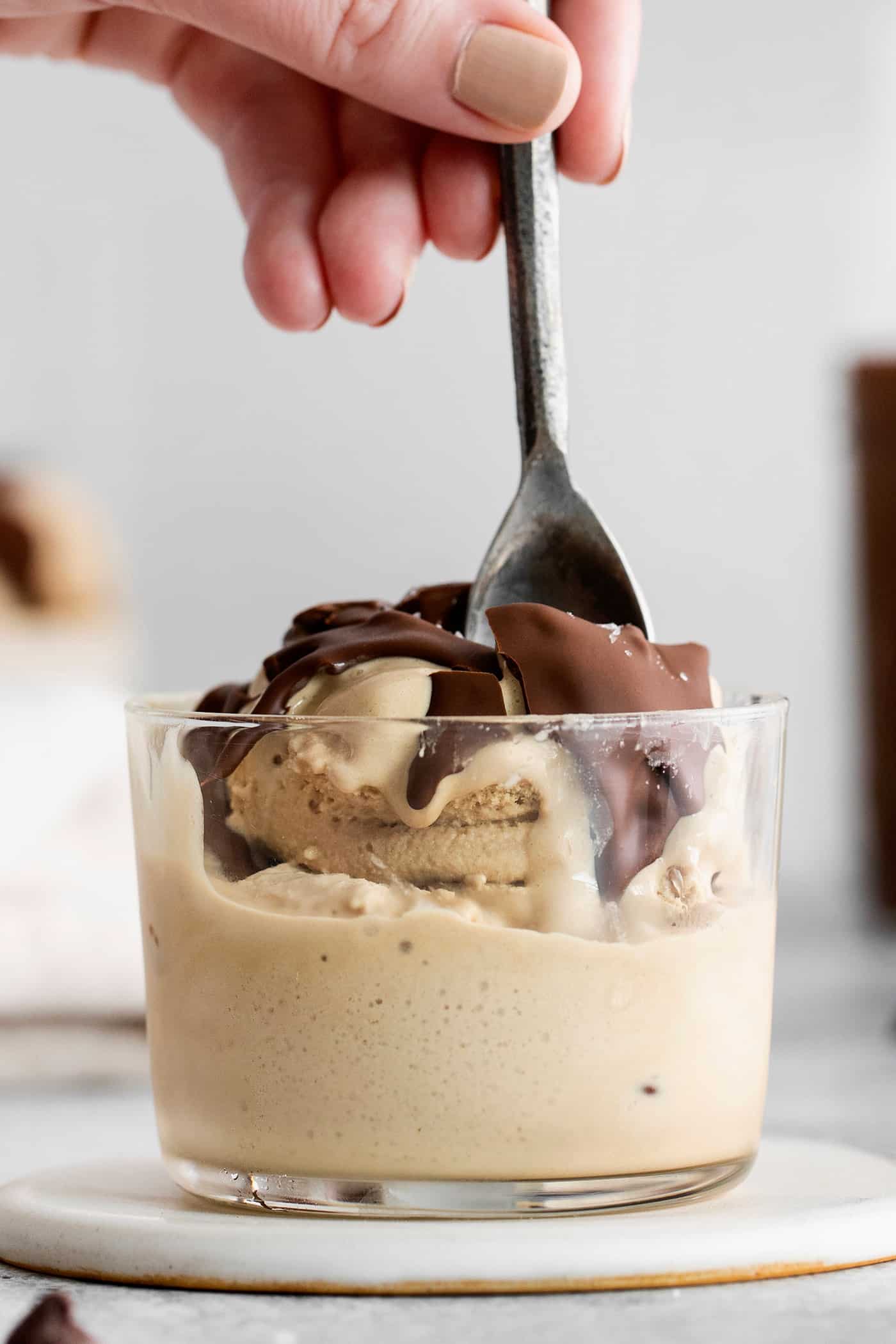 A bowl of ice cream topped with magic shell and a hand holds a spoon.