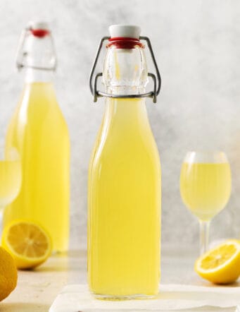 Two bottles of limoncello, two glasses of limoncello, and lemons.