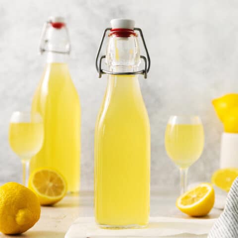 Two bottles of limoncello, two glasses of limoncello, and lemons.