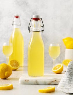 Two bottles of limoncello, two glasses of limoncello, and lemons.