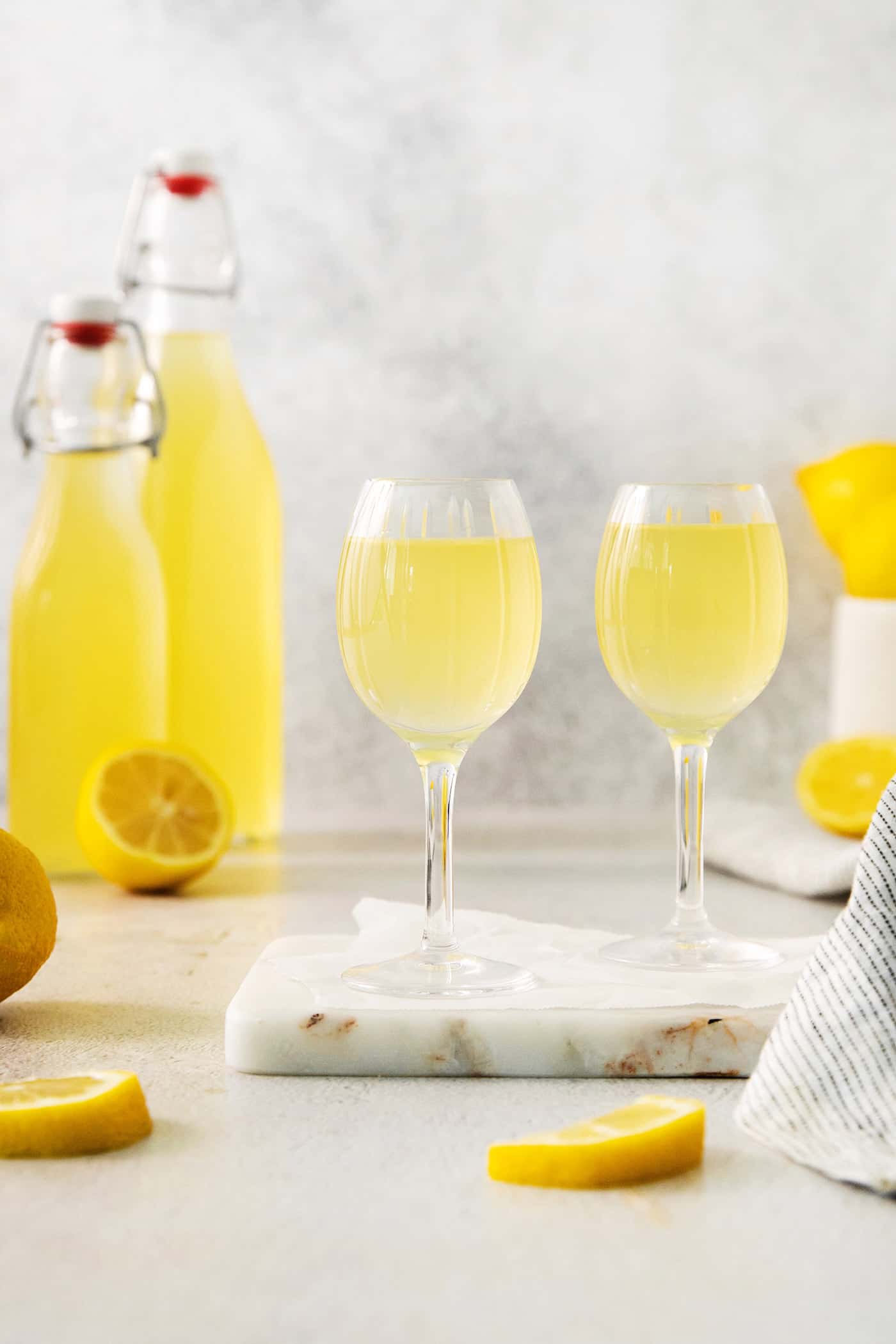 Homemade limoncello in glasses on a marble slabv with a bottle of limoncello in the background.