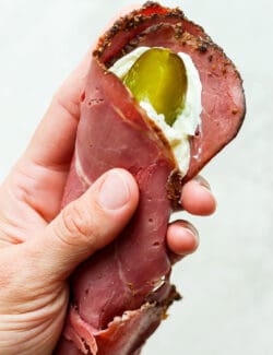 A hand holds piece of ham spread with cream cheese with a pickle inside.