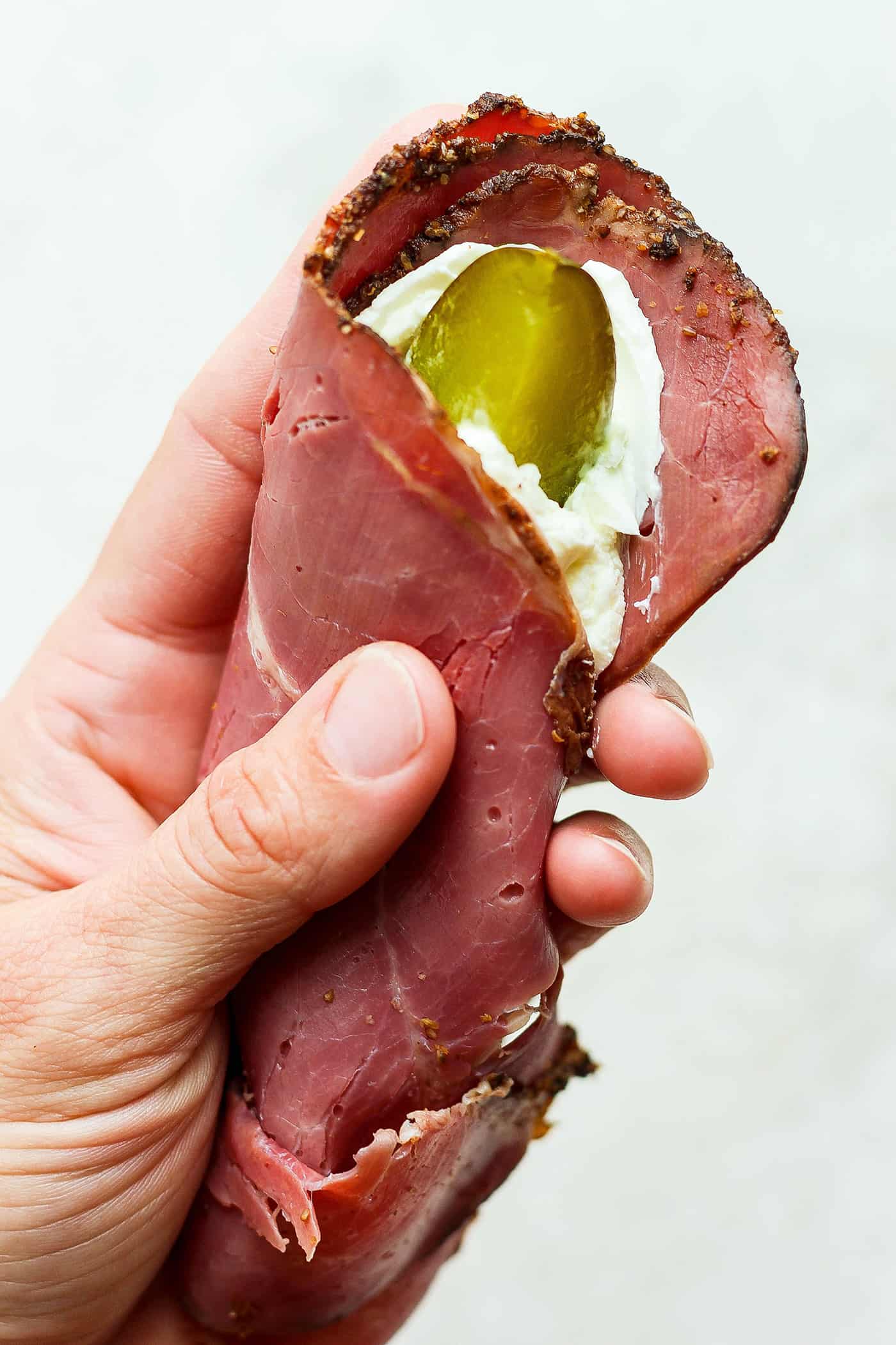 A hand holds piece of ham spread with cream cheese with a pickle inside.