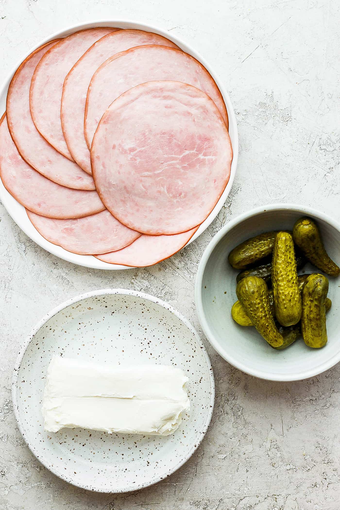 Ingredients for pickle roll ups: sliced ham, cream cheese, and pickles.