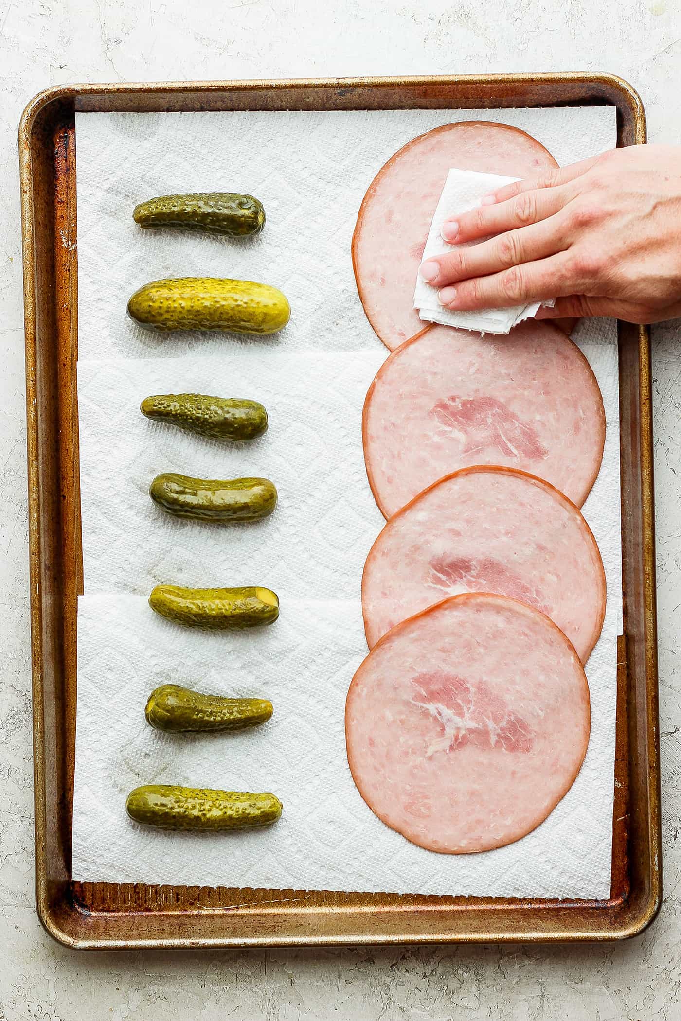 Patting ham dry with pickles next to it.