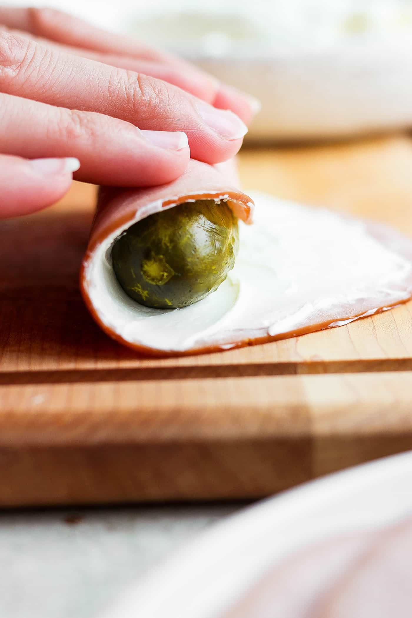 Hands roll a pickle in a piece of ham spread with cream cheese.