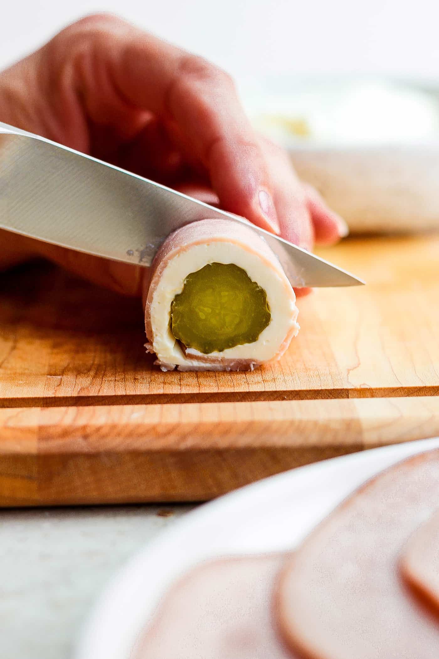 A knife cuts a pickle roll up.