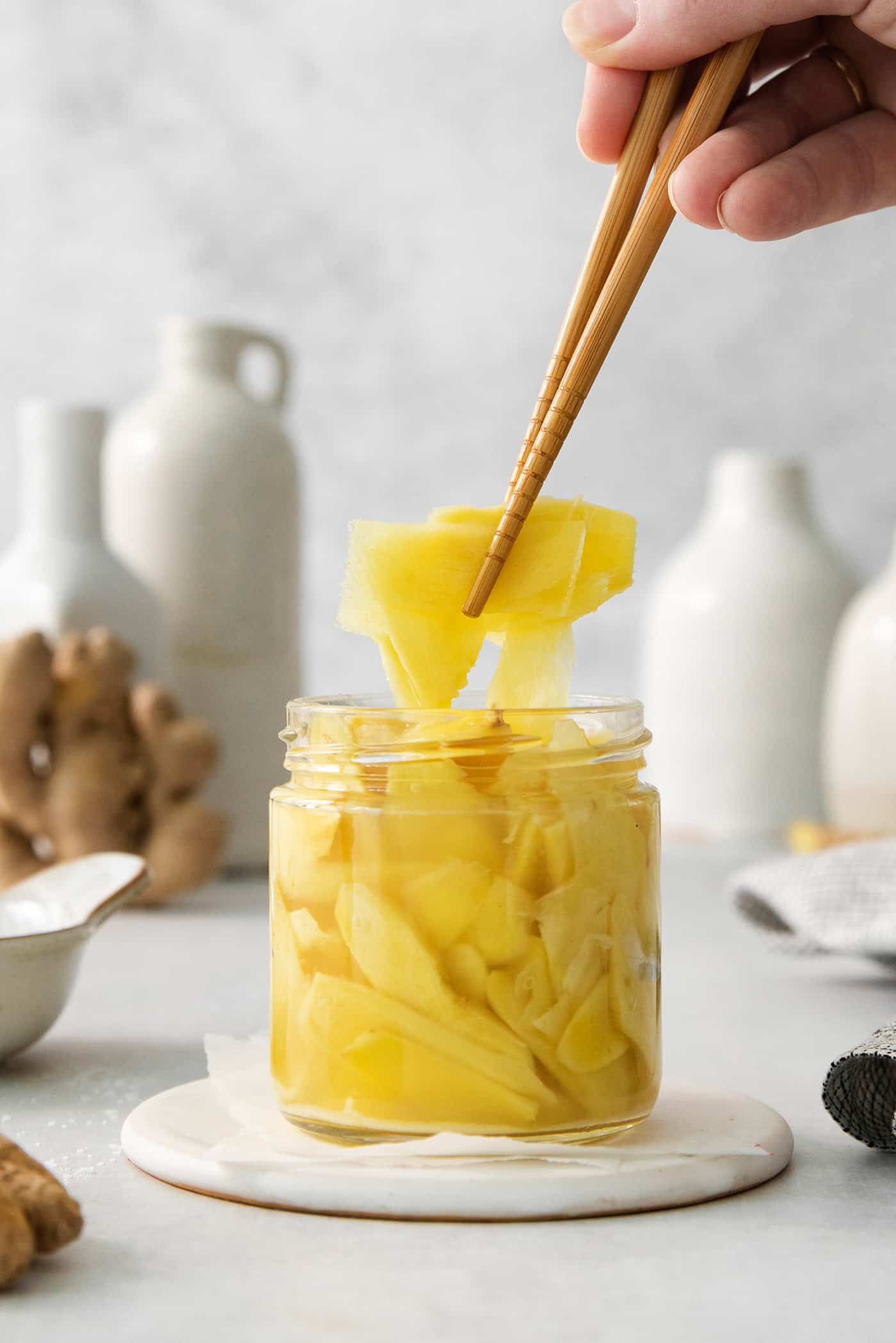 Chopsticks lift out a piece of pickled ginger from a jar.