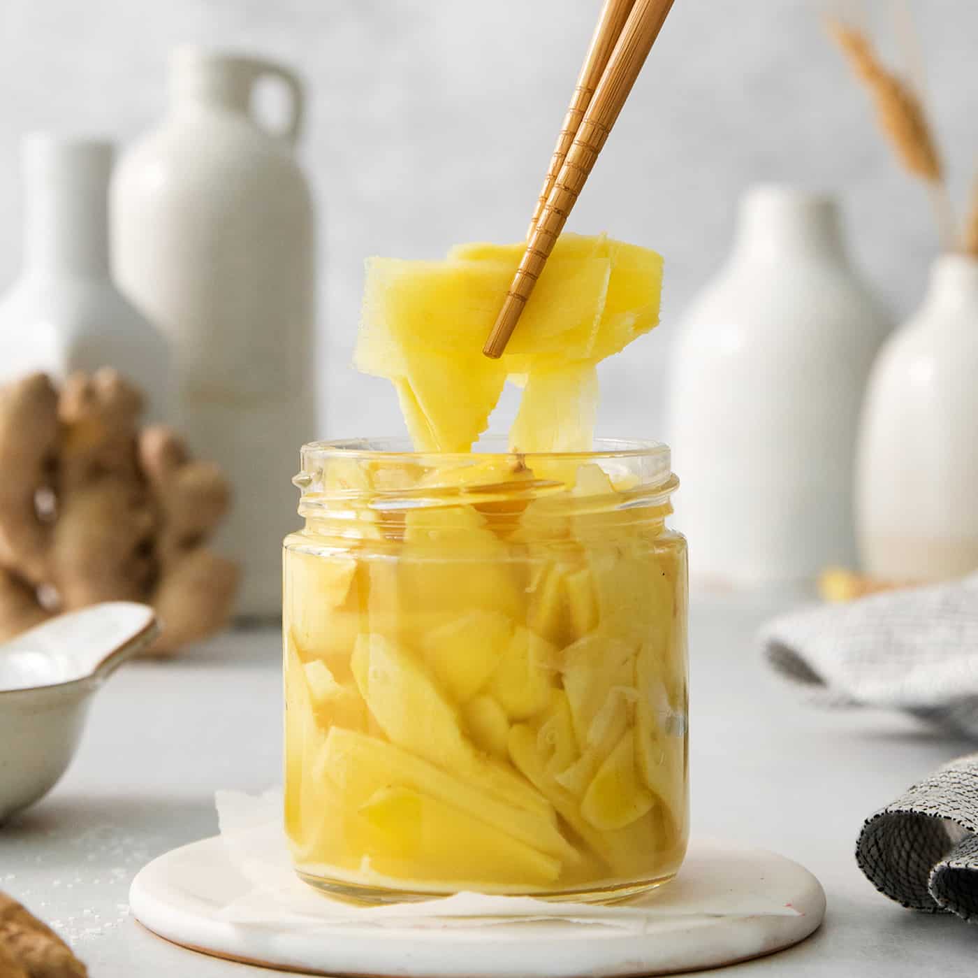 Chopsticks lift out a piece of pickled ginger from a jar.