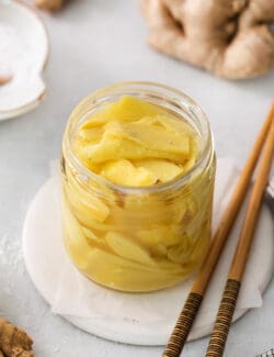 A jar of pickled ginger on a white plate with chopsticks next to it.