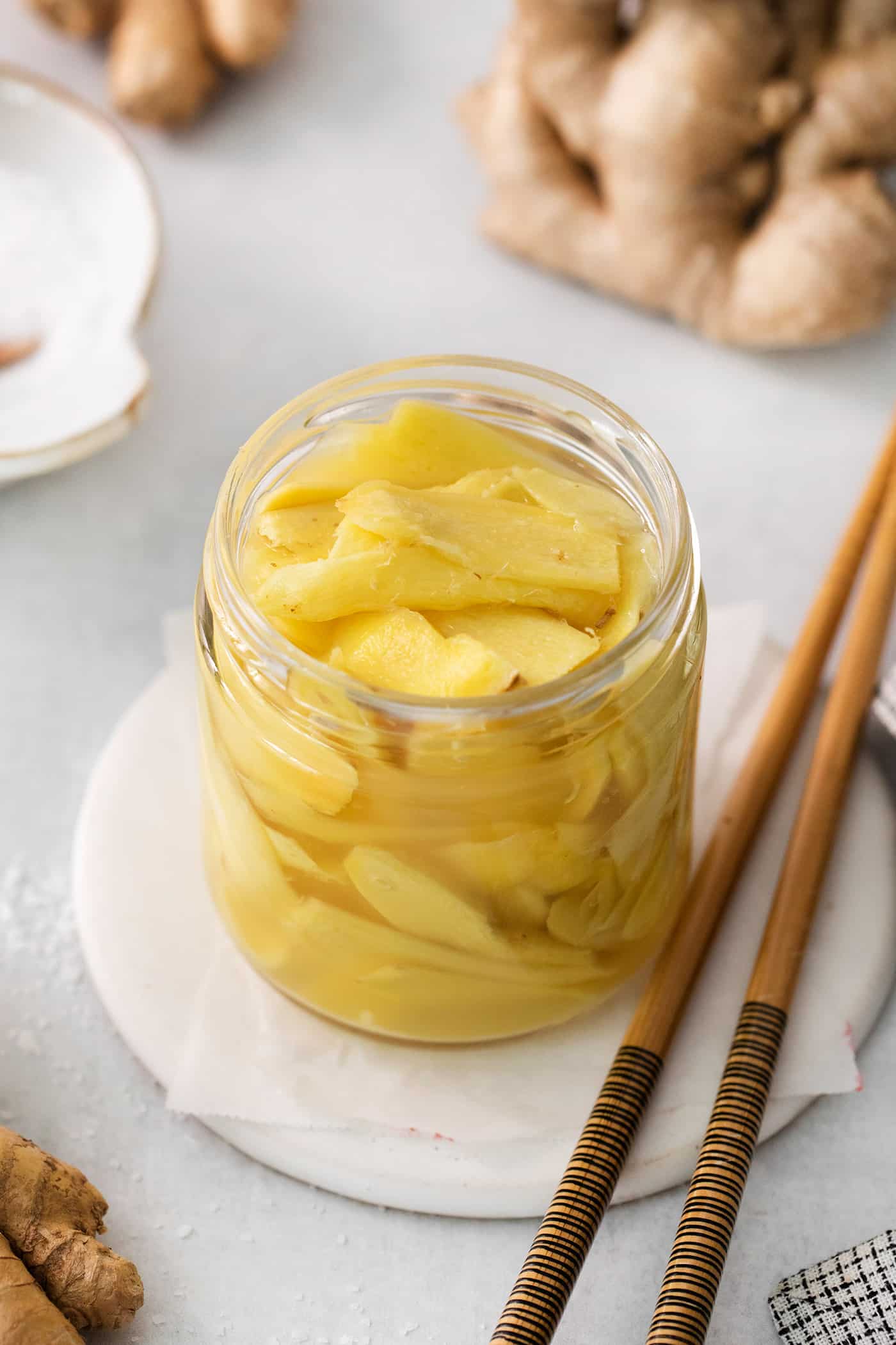 A jar of pickled ginger on a white plate with chopsticks next to it.