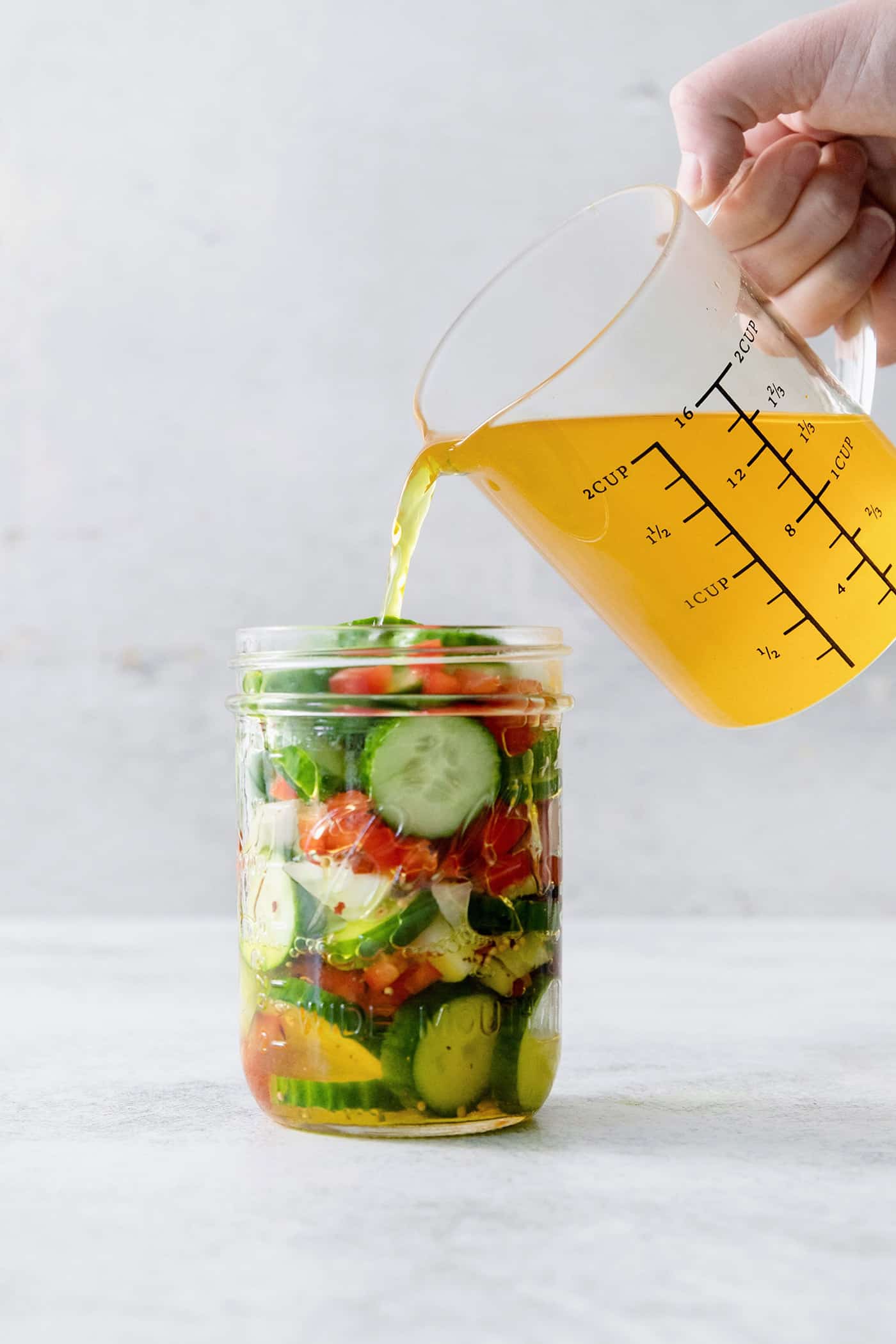 Brine is poured from a pitcher into a jar of vegetables to pickle them.