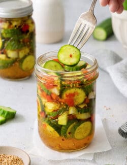 A fork holds a sweet and spicy pickle above a jar.