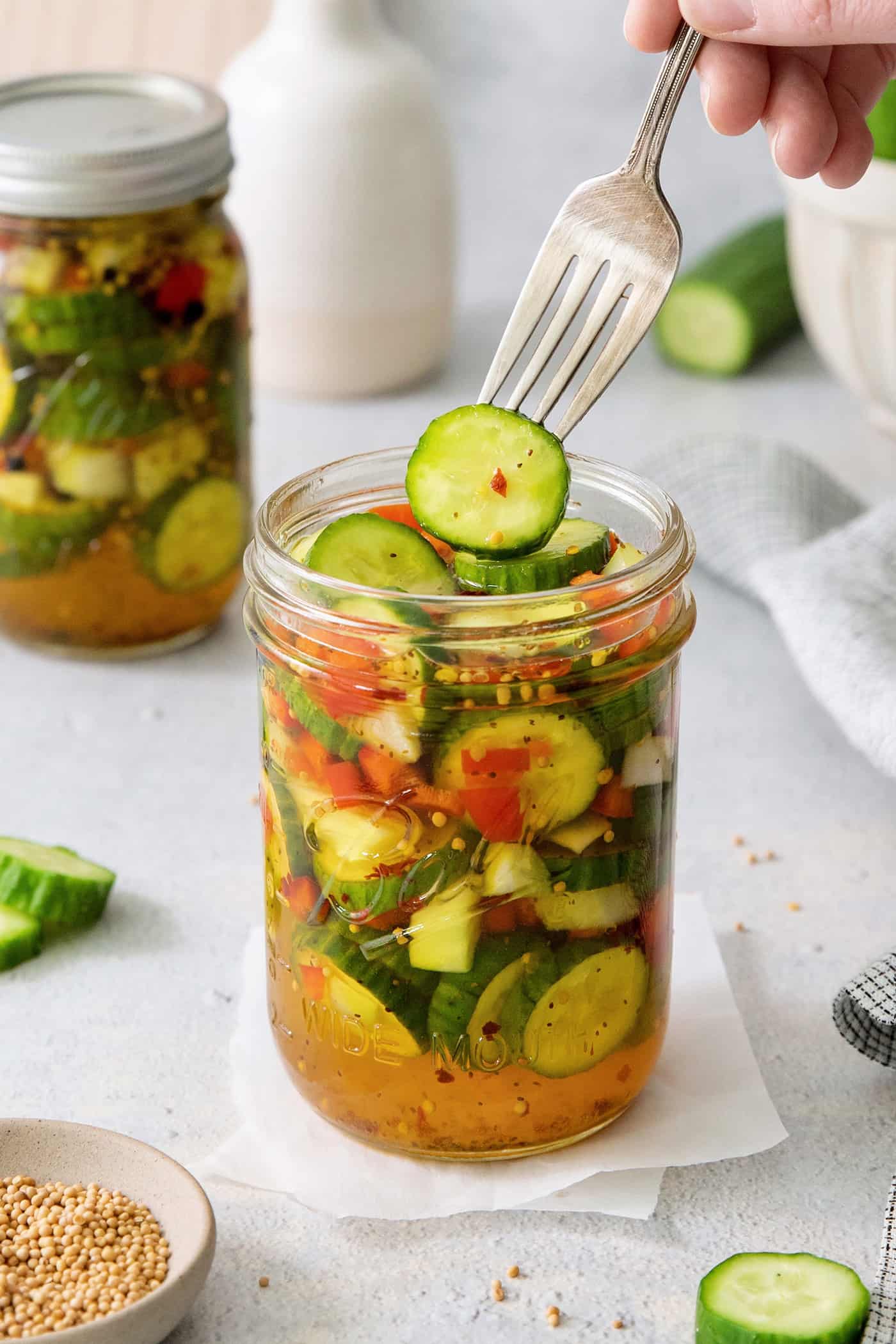 A fork holds a sweet and spicy pickle above a jar.