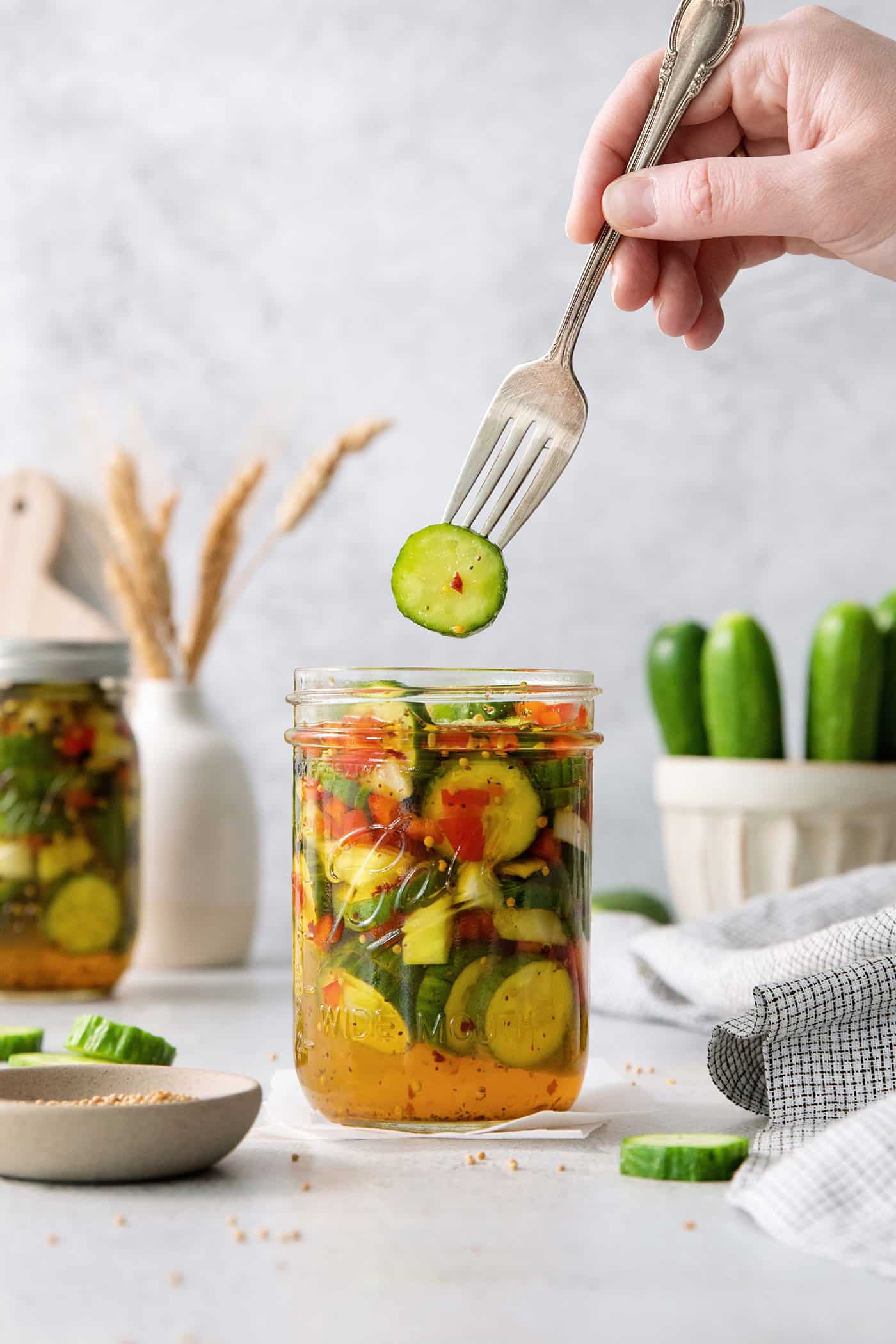 A fork holds a sweet and spicy pickle above a jar.