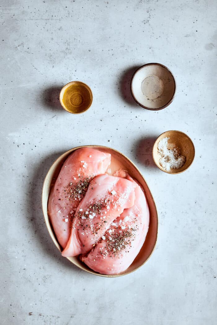 Bowls of chicken, salt, olive oil are seen on a white background.