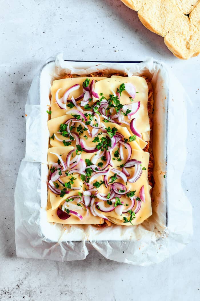 A pan of bbq chicken sliders topped with onions and cilantro.