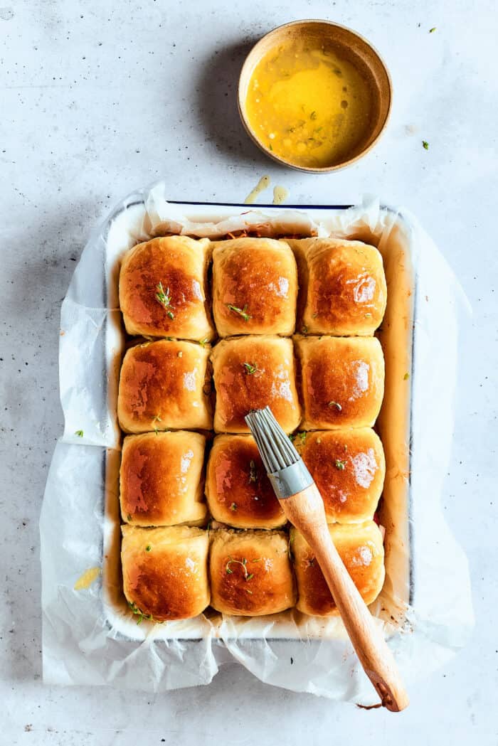 A pastry brush spreads melted butter on top of rolls for bbq chicken sliders.