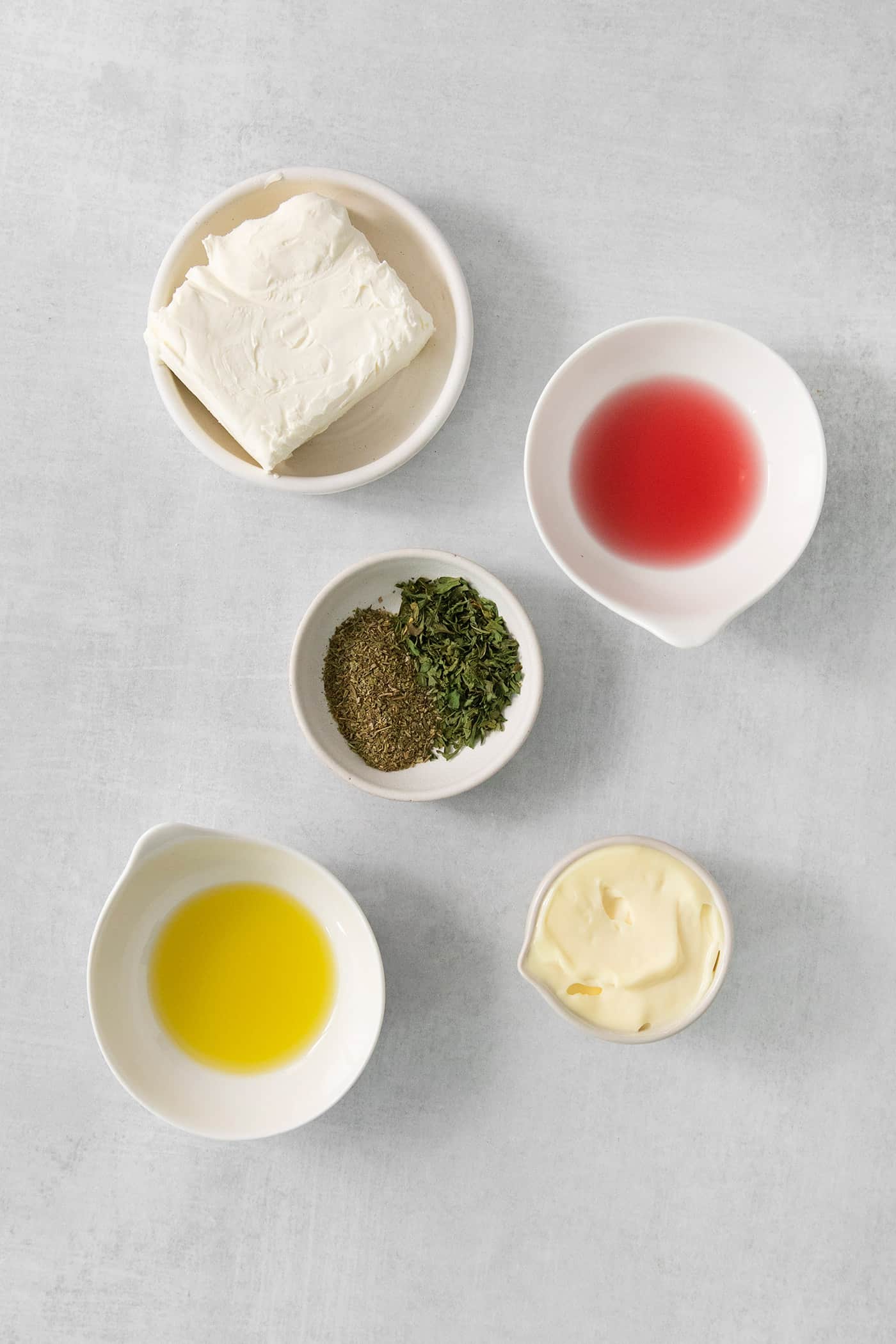 Ingredients for a cream cheese spread are shown in white bowls: cream cheese, red wine vinegar, oil, mayo, and spices.